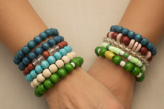Two wrists stacked with colourful handcrafted bead bracelets by BeadCandi - greens, purples, blues and naturals on linen
